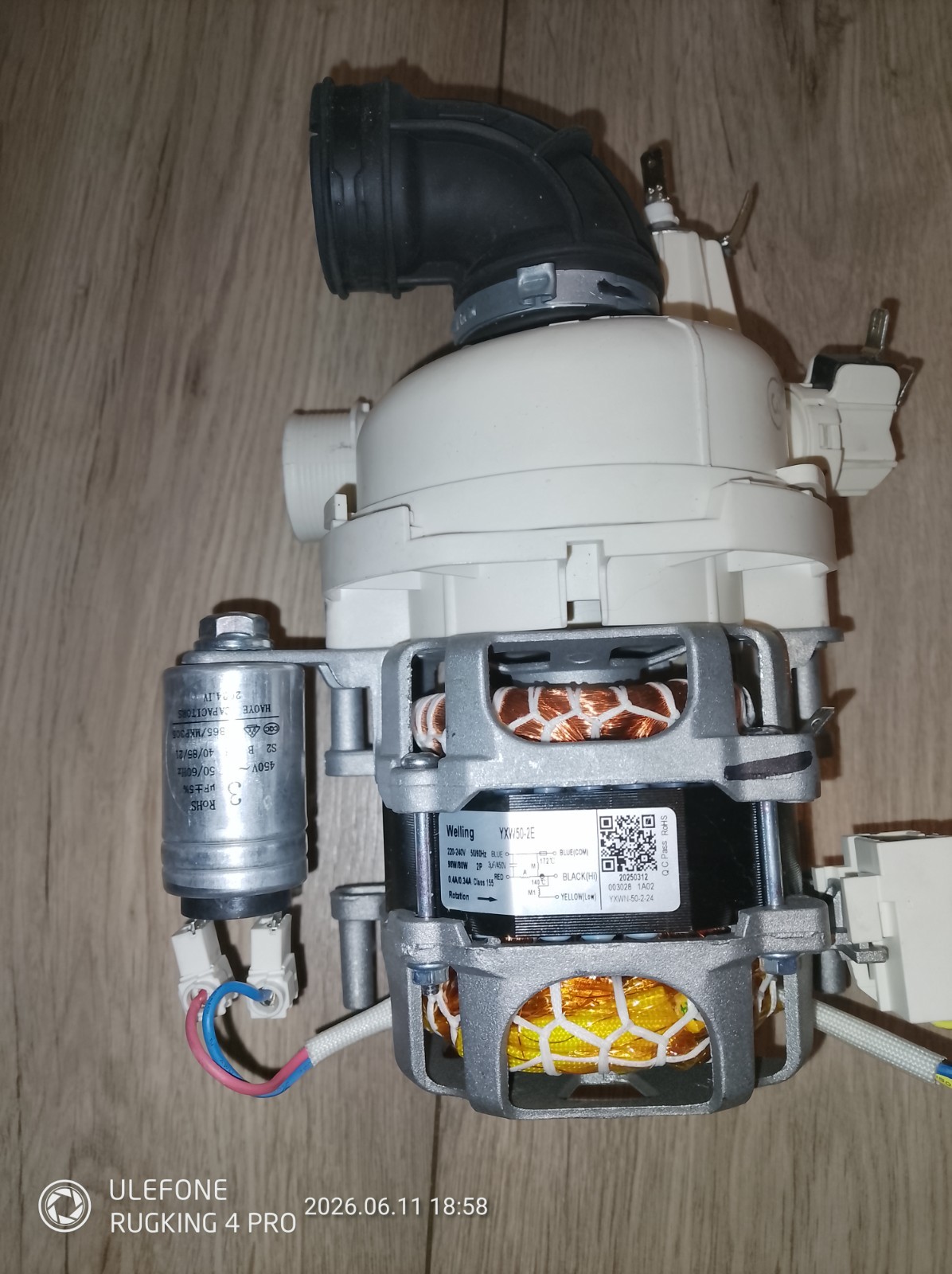 s-l1600-1078.jpg Motor pump assembly with white plastic housing and visible copper windings in a gray metal frame, mounted on a wooden floor. A black elbow pipe attaches to the top, with electrical wires and a small silver capacitor nearby. The label on the motor shows model information.