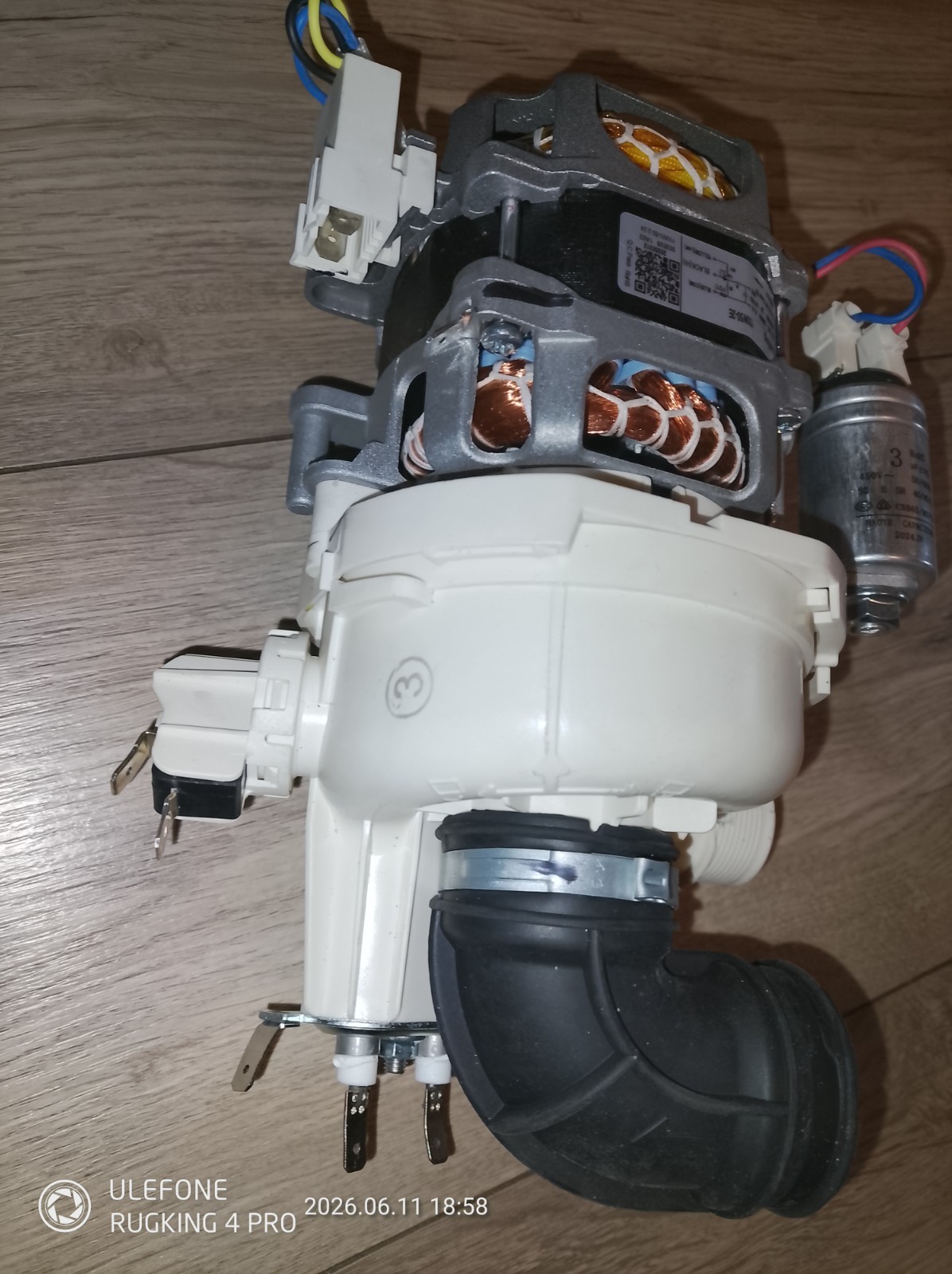 s-l1600-1080.jpg Disassembled electric motor or appliance drive unit with copper windings, white plastic housing, wiring harnesses, and a capacitor laid on a wooden floor as seen from the side view, showing internal components.