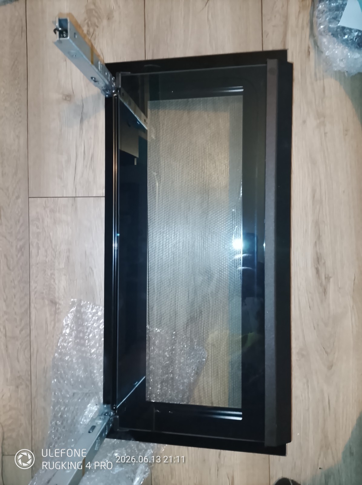 s-l1600-1140.jpg Black glass oven door with metal frame resting on a wooden floor, partially unpacked with bubble wrap seen nearby.