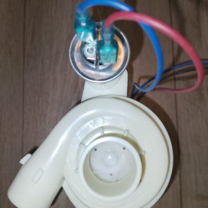 Disassembled ceiling light socket with blue and red wires connected to a green terminal on a metal plate, on a wooden floor.