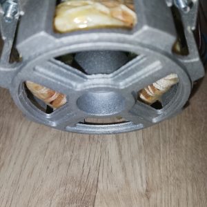 Close-up of a small electric motor rotor, copper windings visible inside a gray metal housing on a wooden surface.