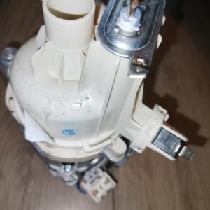 Close-up of a white plastic valve assembly with a metal contact and small electrical connectors, likely part of a plumbing or pump device.