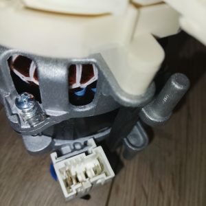 Close-up of a small motor showing copper windings, a white connector, and a gray mounting bracket.