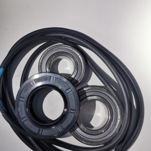 Coiled black cable beside two metal bearing races on a white surface.