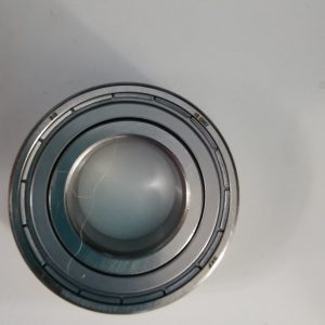 Close-up of a metallic camera lens mount with an inner glass element on a light surface, showing concentric rings.