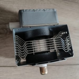 Close-up of a metal electrical component with zigzag metal springs inside a rectangular box and a copper tube extending downward.