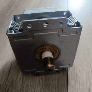 Close-up of a small metal gearbox or motor housing with a protruding shaft and visible copper winding at the base, resting on a wooden floor.