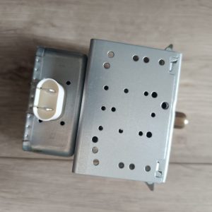 Metal electrical transformer with a perforated cover and a white plug-in socket on the side (informational).
