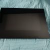 Closed black laptop resting on a teal quilted surface, with a metal stand visible at the right edge.