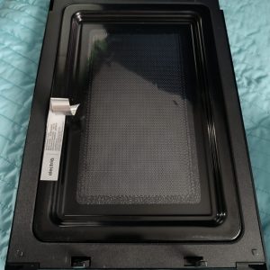 Black metal frame of a microwave oven door with an inner glass panel, placed on a blue quilted surface
