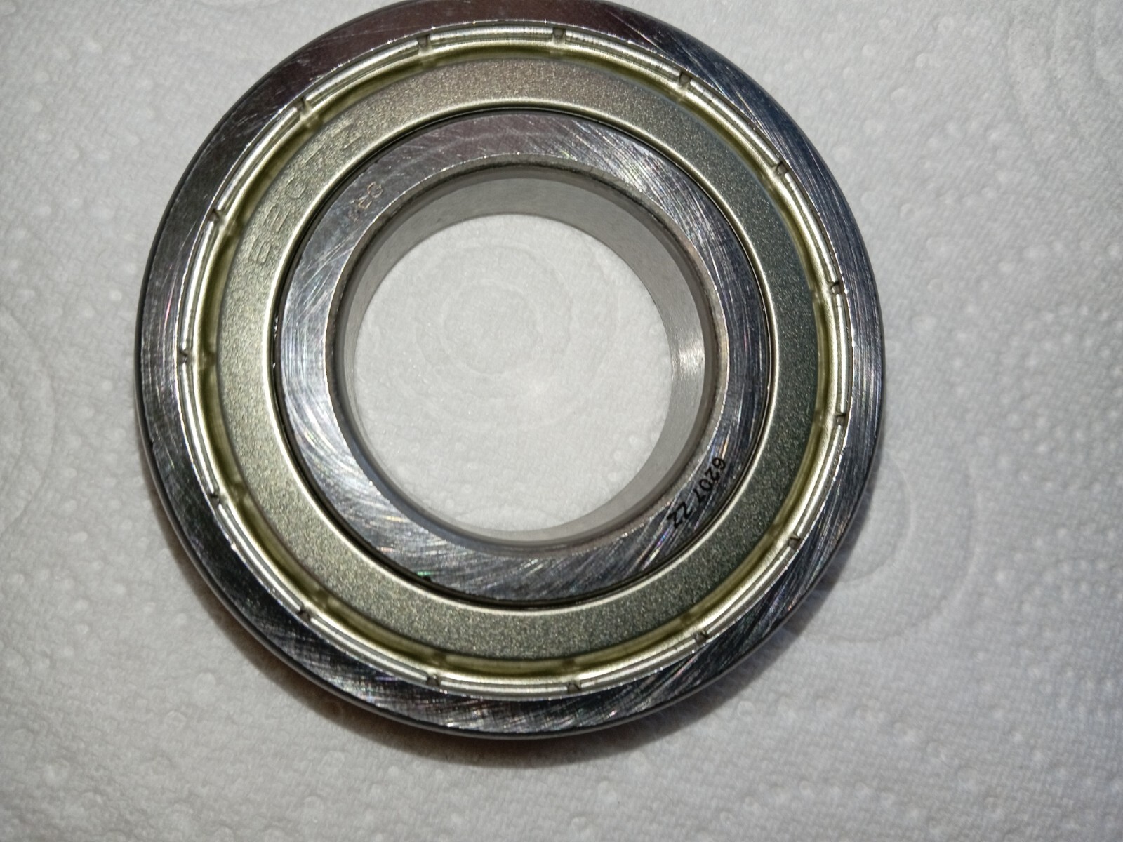 s-l1600-133.jpg Close-up of a metal bearing race with inner and outer rings on a light background.