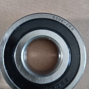 Close-up of a sealed ball bearing (6306-2RS) with inner and outer rings and black seal, resting on a brown surface