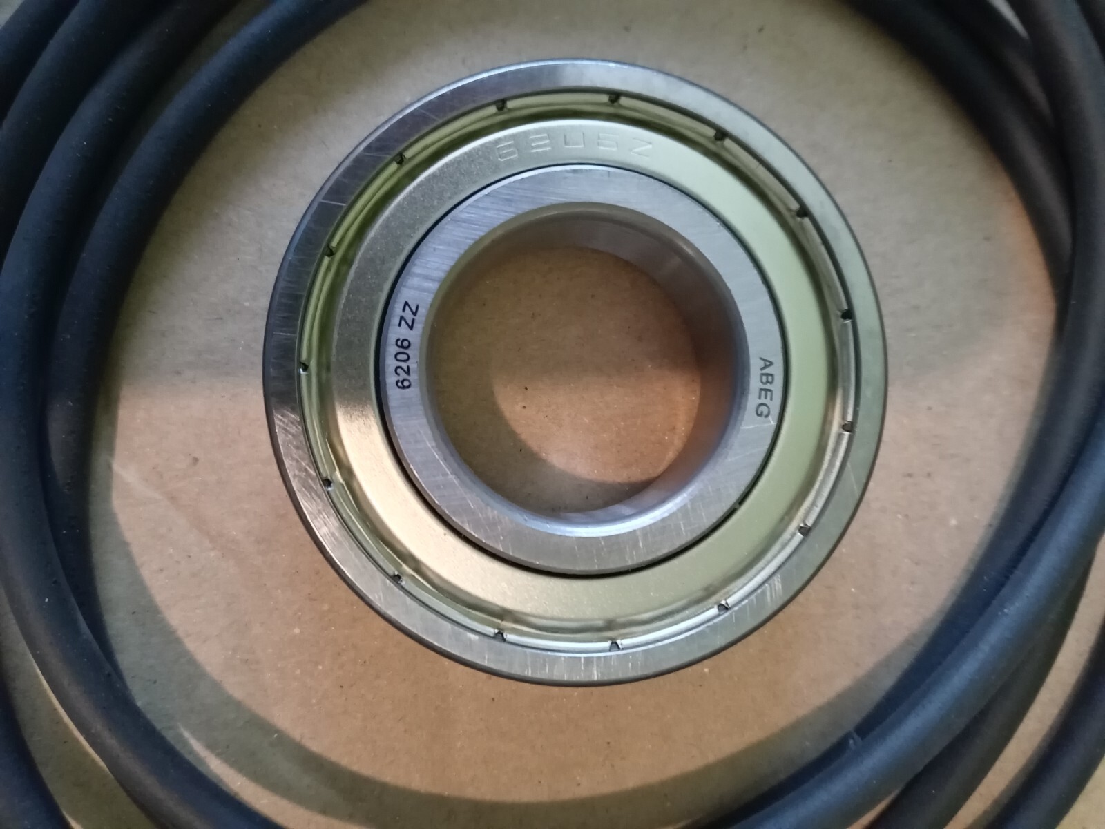 s-l1600-170.jpg Close-up of a metal ball bearing (6206 ZZ) with inner and outer race visible on a brown surface. A black cable surrounds it.