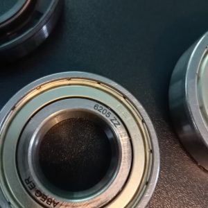 Close-up of metal lens bearings with stamped numbers (6205 ZZ) and grooves, on a dark surface.