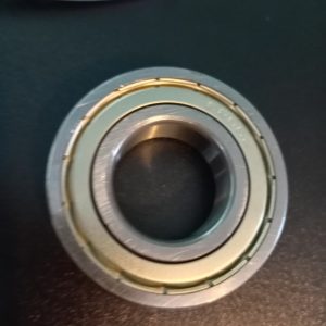 Close-up of a metallic ball bearing with inner and outer races resting on a dark surface.