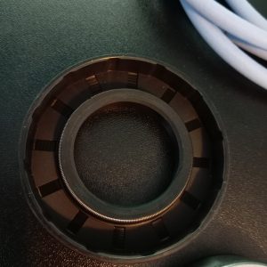 Close-up of a circular black lens-mount ring with gear-like notches on a dark surface; a light-blue cable sits in the corner.