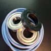 Close-up of metal ball bearing races with a black rubber seal resting on a coiled blue hose against a dark background