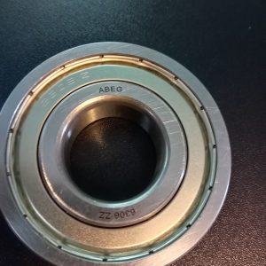 Close-up of a round metal bearing with inner and outer races resting on a dark surface, markings visible on the race (ABEG).