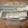 White plastic appliance component with multiple internal slots and a hinged/removable section, photographed on bubble wrap.