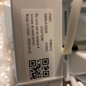 Close-up of a gray plastic device with a white label showing a product code, caution text, origin, and a QR code.