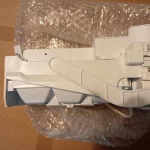 Close-up of a white plastic mechanical part with a curved arm and an on/off switch, resting on bubble wrap in a box