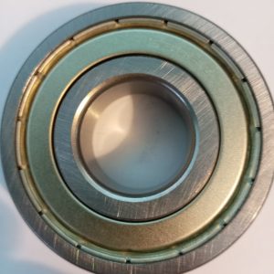 Close-up of a metal ball bearing with inner and outer rings and a green seal, resting on a white surface.”, “Macro shot of a circular ball bearing showing its concentric rings (inner bore and outer race) used in machinery.”, “Close view of a precision bearing component from a mechanical assembly.”
