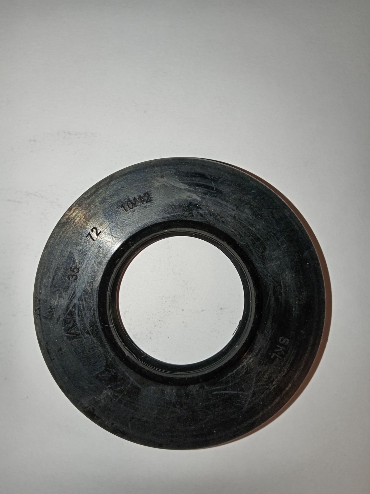 s-l1600-282.jpg Circular black gasket with inner bore resting on a white surface, showing etched numbers on the edge (machinery seal).**