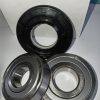 Set of three ball bearings on a white surface in front of a white box with blue print; two silver bearings and one black-coated bearing visible from the front.