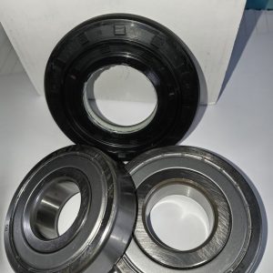 Set of three ball bearings on a white surface in front of a white box with blue print; two silver bearings and one black-coated bearing visible from the front.