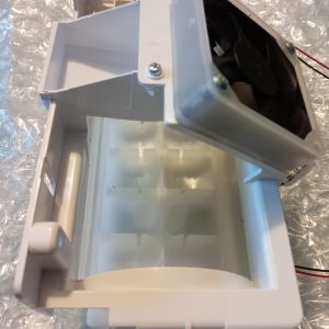 White plastic blower/duct assembly with a small internal fan and mounting screws, showing an open cavity and brackets behind a bubble wrap-like background.