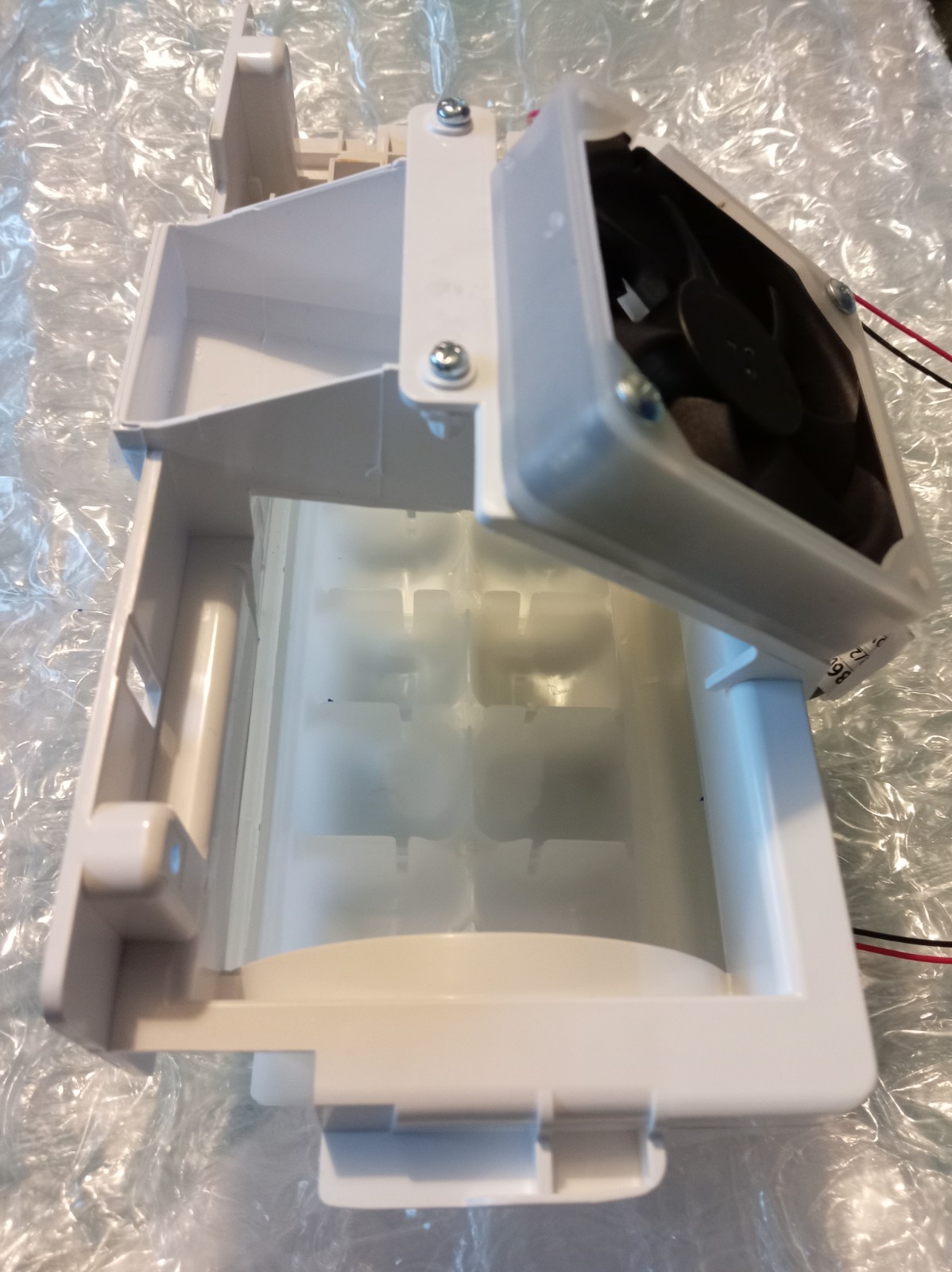 s-l1600-363.jpg White plastic blower/duct assembly with a small internal fan and mounting screws, showing an open cavity and brackets behind a bubble wrap-like background.
