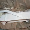 White plastic lever/arm assembly with a mounting bracket on brown paper, likely part of an appliance mechanism