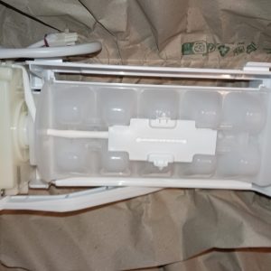 White plastic appliance component with six rounded mold pockets and a central mounting piece, laid on brown paper.