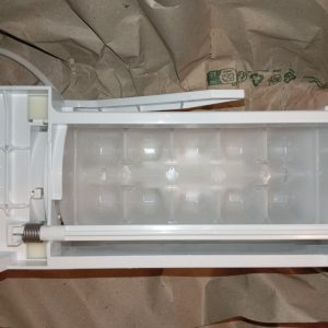 Open white plastic appliance part with a large internal cavity and a spring-loaded rod, placed on brown paper.