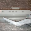 White plastic appliance component with a long rectangular body on bubble wrap, incl. an angled support arm.