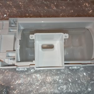 White plastic appliance part with a hollow center and mounting tabs placed on bubble wrap, photographed from above; likely an internal housing component.