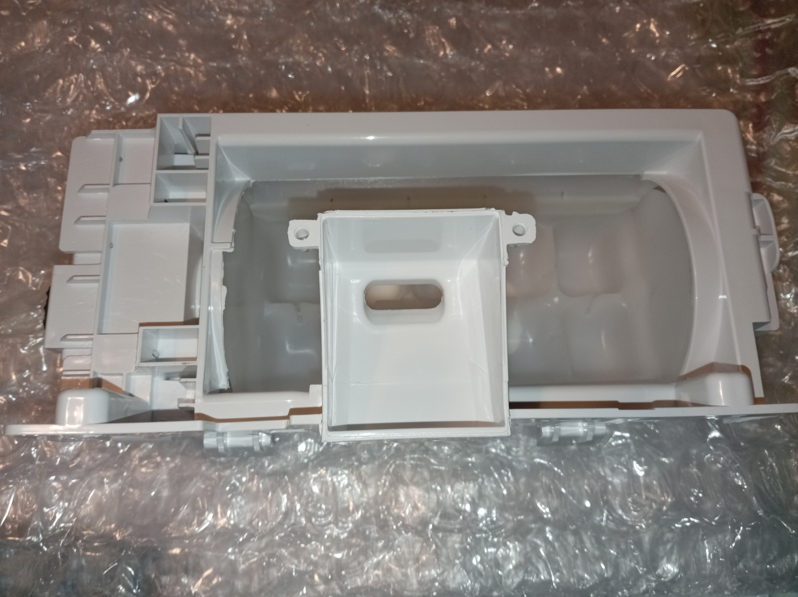 s-l1600-381.jpg White plastic appliance part with a hollow center and mounting tabs placed on bubble wrap, photographed from above; likely an internal housing component.