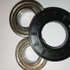 Close-up of metal bearing races and a black plastic seal laid on a white surface