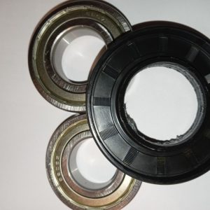 Close-up of metal bearing races and a black plastic seal laid on a white surface