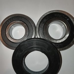 Three metal ball bearings laid on a white surface, showing inner race openings and outer rings in different finishes.