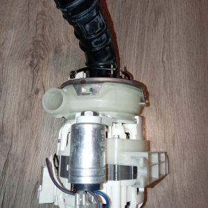 Disassembled appliance pump with a black flexible outlet hose, white plastic housing, metal motor, and blue wires on a wooden floor