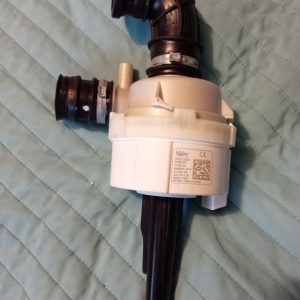 White garbage disposal unit with black inlet/outlet pipes mounted under a sink, resting on a light-blue quilted surface.