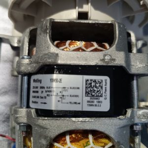 Close-up of a small electric motor with exposed copper windings inside a gray metal frame and white plastic housing.