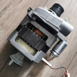 Close-up of a disassembled electric motor showing copper windings and plastic housing on a wooden surface.