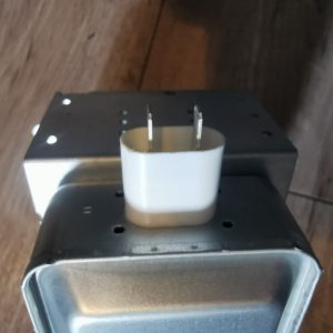 Close-up of an electrical transformer with two flat blade prongs protruding from a white plastic spacer on a metal housing.