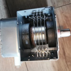 Close-up of the inside of a small metal device: cylindrical rollers, a wire rack above them, and a small shaft on the right side inside a rectangular housing.