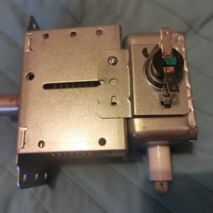 Close-up of a metal electronic module with a round rotary knob and mounting brackets, likely a car stereo component.