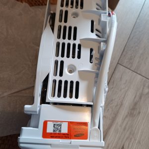 Back view of a white appliance with numerous vertical vent slots and an orange label on the side, resting on a floor.