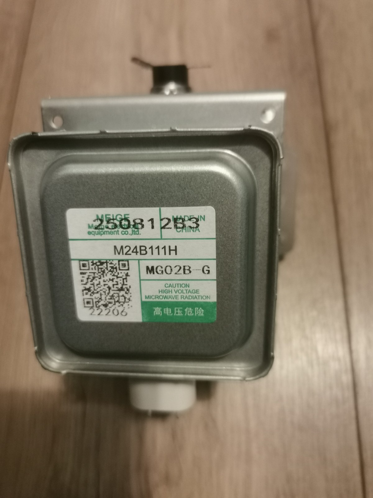 s-l1600-660.jpg Metal electrical transformer with a green-labeled sticker reading M24B111H and a caution about high voltage microwave radiation, on a wooden floor