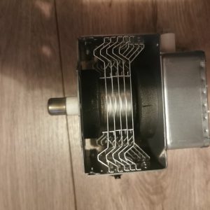 Close-up of a small metal mechanical assembly with a bundle of vertical metal fins and a right-side metallic housing, mounted on a wooden floor surface.